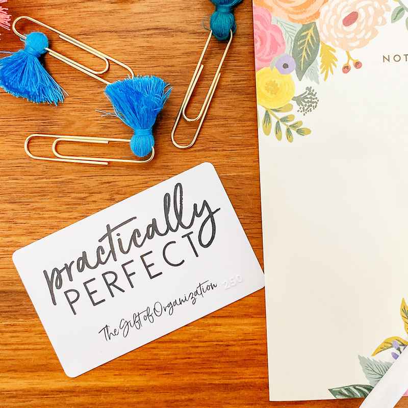 Image Description: A Practically Perfect gift card lays on a wooden surface next to a notepad