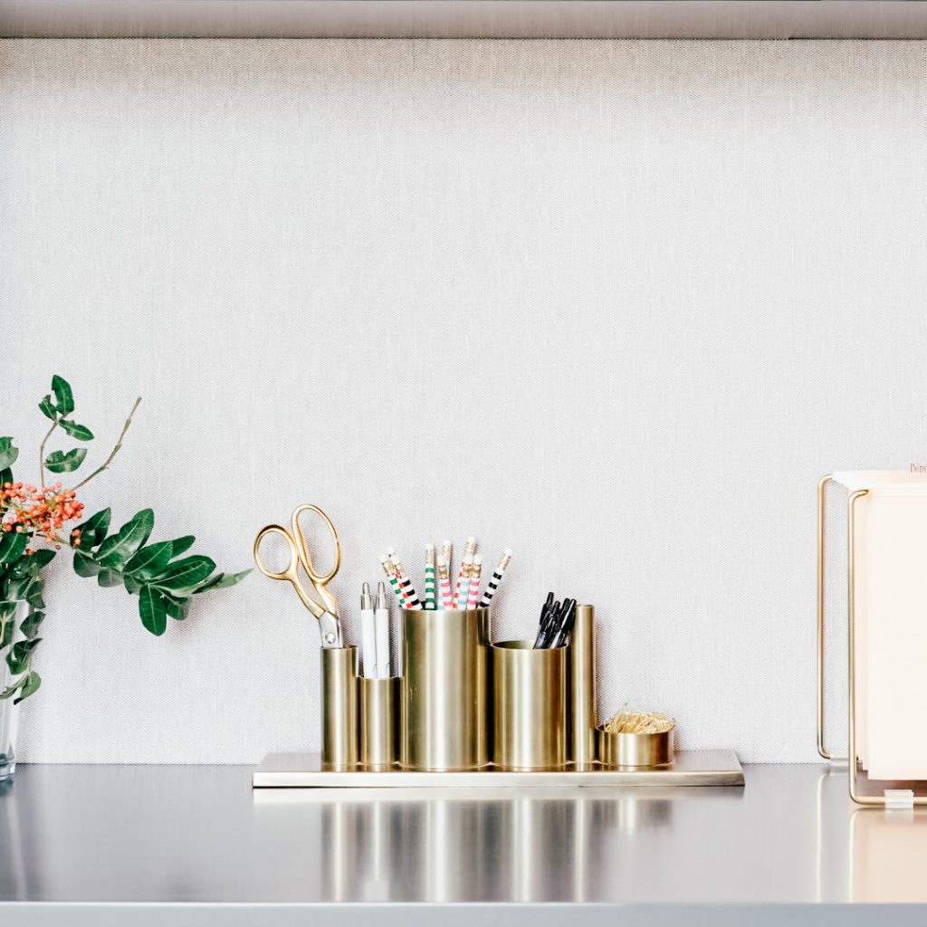Image Description: A gold desk organizer filled with writing utensils sits between a vase of flowers and a file holder.
