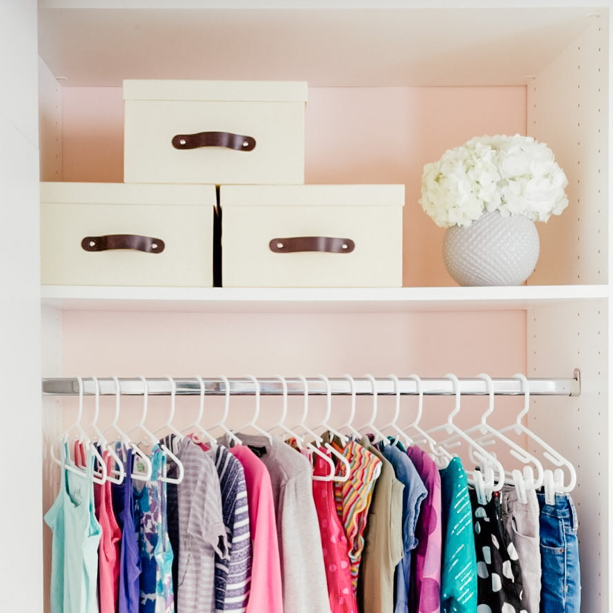 Image Description: Three linen storage boxes sit neatly above a row of hanging children's clothing