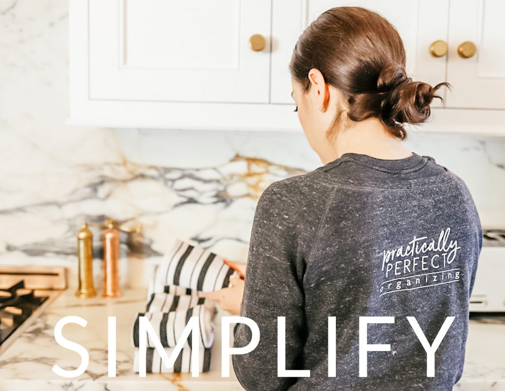 Image Description: An organizer in a gray sweatshirt with her back facing us folds striped kitchen towels.