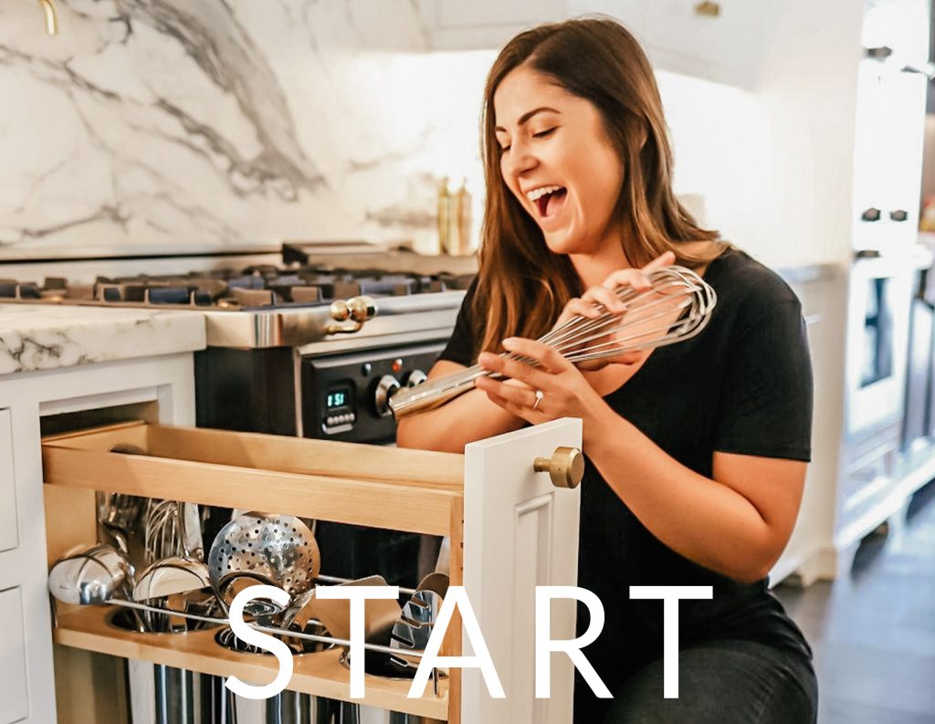 EmplImage Description: An organizer in all black laughs while holding a whisk. A pull-out drawer with divided cooking utensils is in front of her.