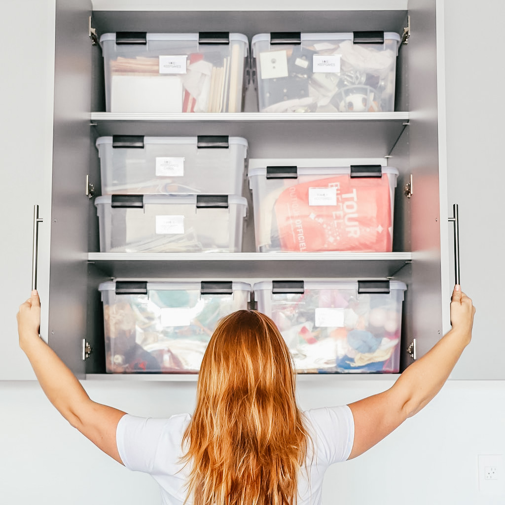 Image Description: A woman with long hair stands in front of a garage cabinet filled with sturdy, labeled totes