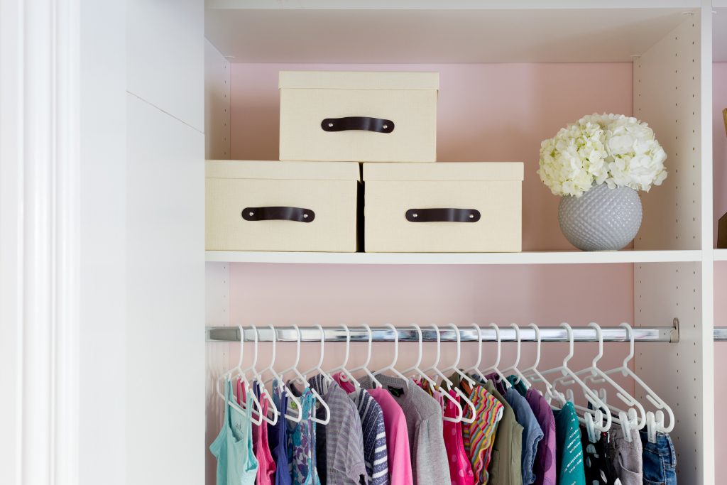 Image Description: Three linen storage boxes sit neatly above a row of hanging children's clothing