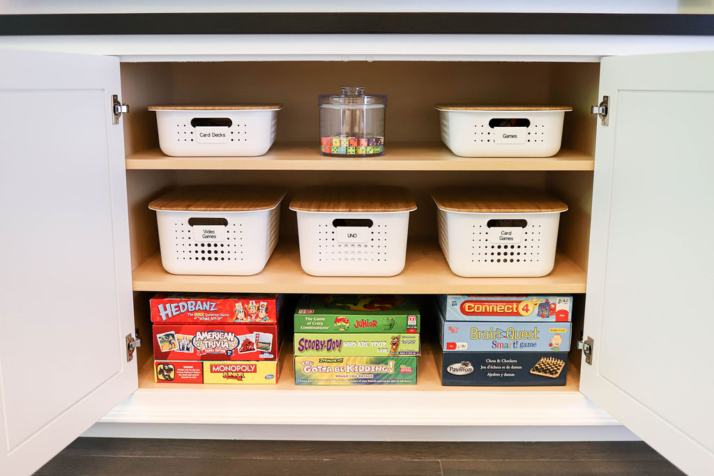 Image Description: White, labeled bins sit above a stack of organized board games in a cabinet.