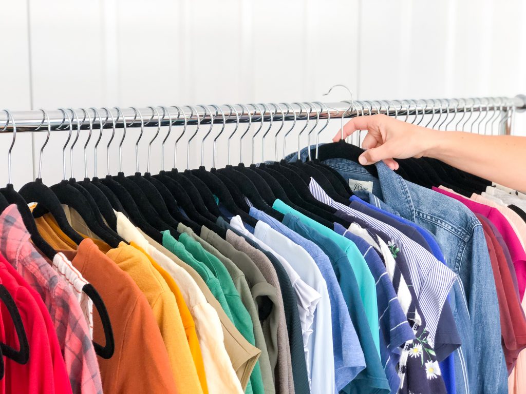 Image Description: A row of color-coded clothing hangs on a clothing rack, a hand holds one hanger out