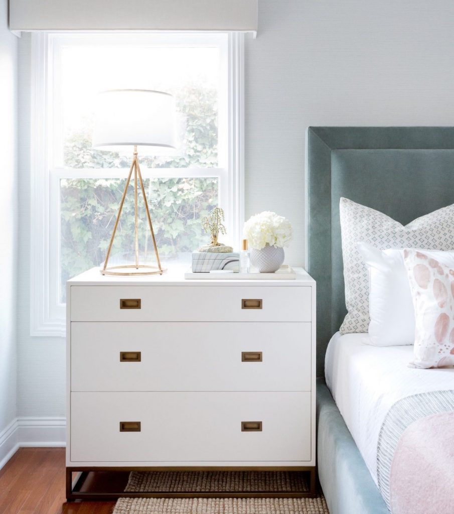 Image Description: A lamp, air plant and white flowers sit on a crisp, white bedside table.